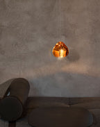 One amber glass head from this Clérachic pendant glows against a rough concrete wall above a low dark sofa.