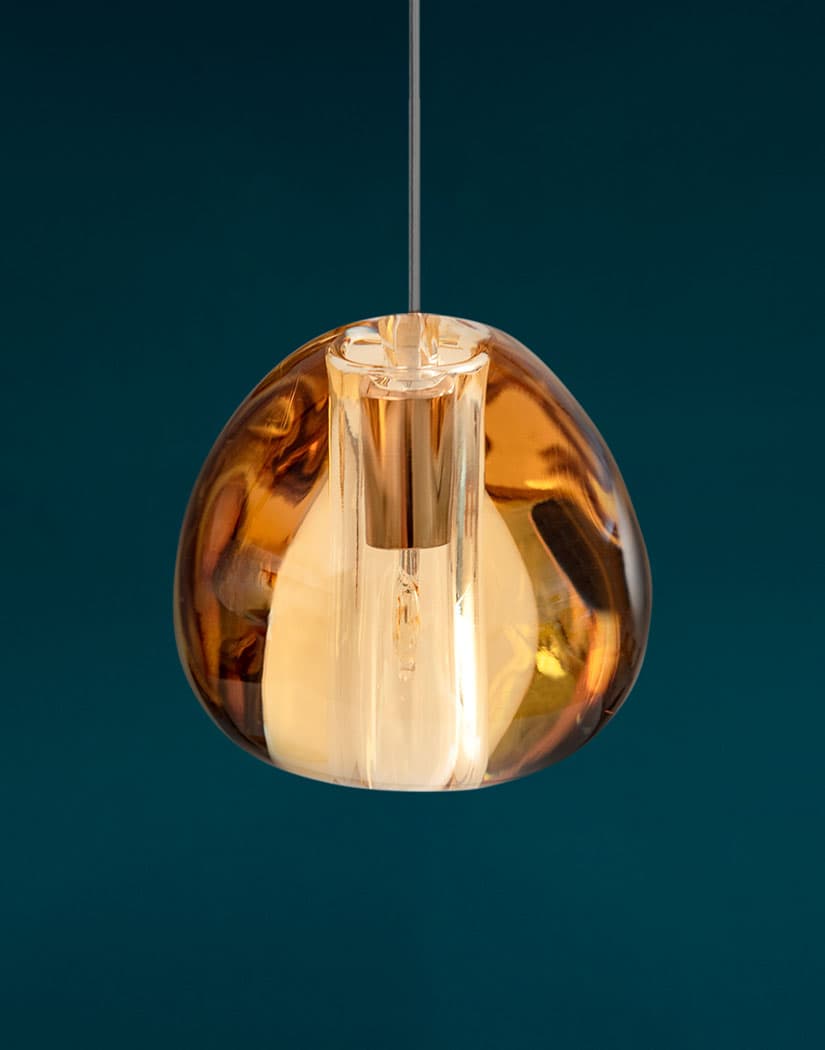 Close view of a copper-toned amber glass head on this Clérachic pendant, shown against a deep teal backdrop.