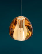 Close view of a copper-toned amber glass head on this Clérachic pendant, shown against a deep teal backdrop.