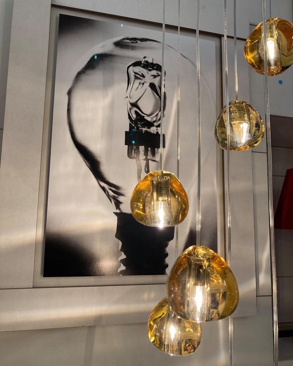 Yellow-amber glass heads of this Clérachic pendant glow in front of a huge black-and-white print of a light bulb.