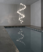 A spiral column of clear glass heads on this Clérachic pendant hangs over a long, still indoor pool in a plain concrete room.
