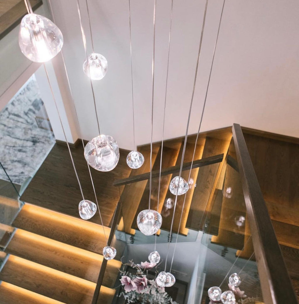 Looking down onto a timber stair with lit treads, a Clérachic pendant's clear glass heads dangle on long wires.