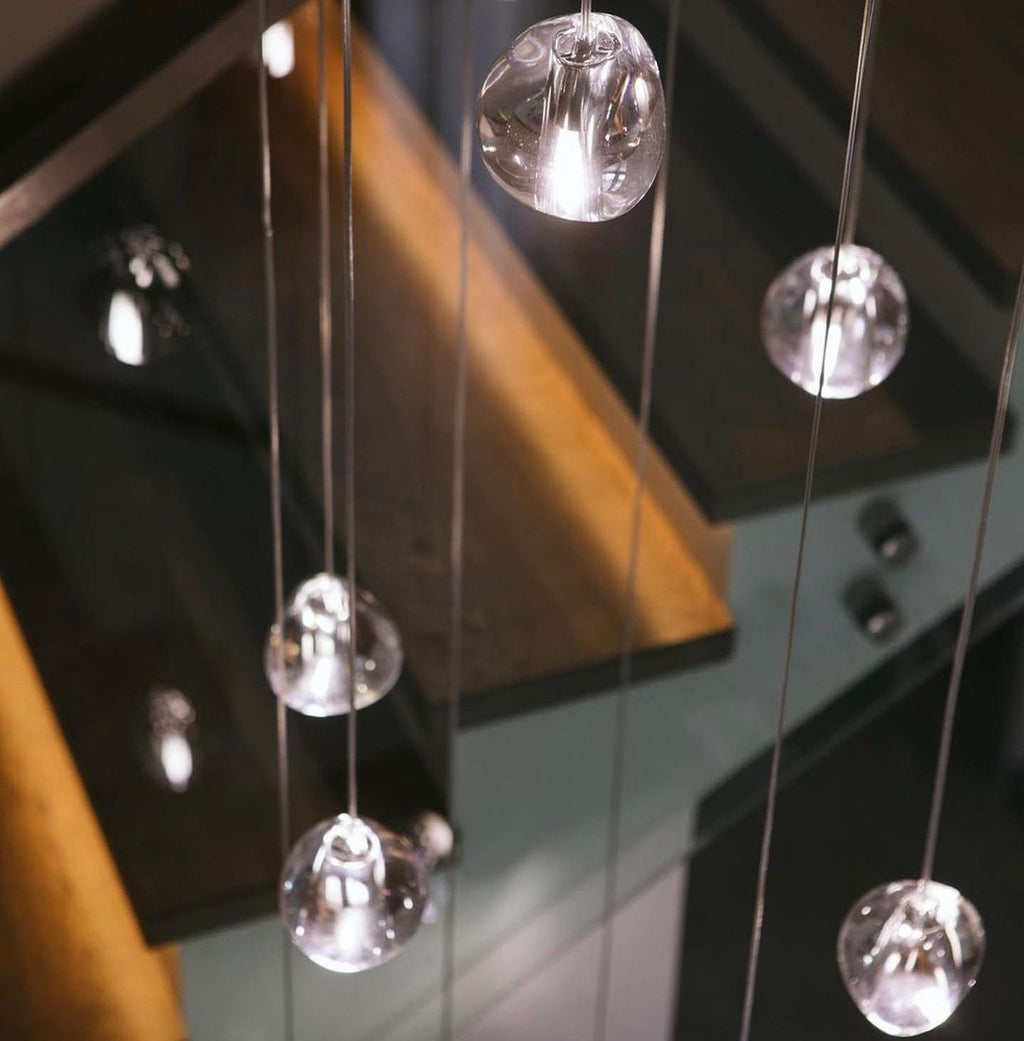 Close view of clear glass heads on this Clérachic pendant, hanging past the wooden treads of a staircase.