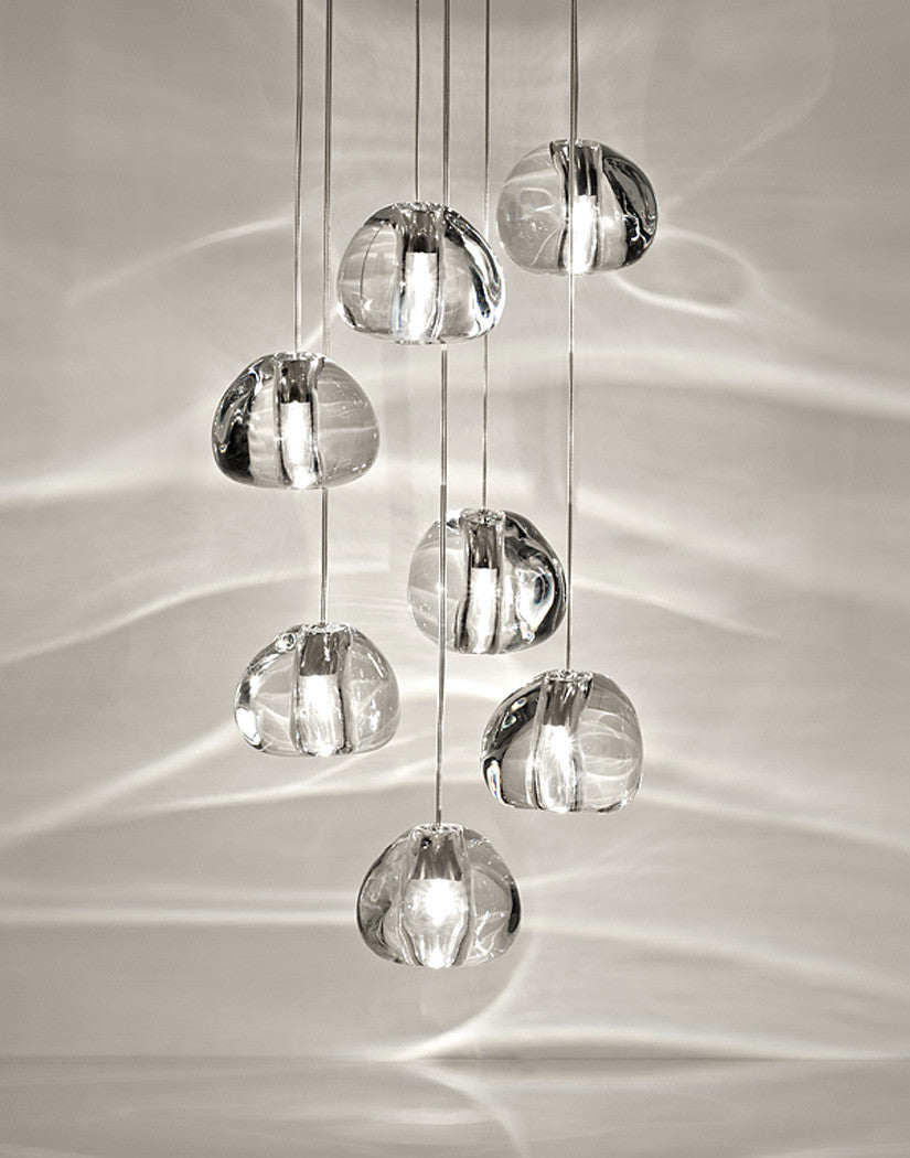 Seven clear glass heads of this Clérachic pendant hang close together, with the light rippling across a pale wall behind them.
