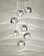 Seven clear glass heads of this Clérachic pendant hang close together, with the light rippling across a pale wall behind them.
