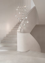 This Clérachic pendant hangs as a cluster of clear glass heads, high above a white staircase with a curved wall.