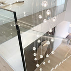 Clear glass heads of this Clérachic pendant hang beside a glass balustrade, over a pale wood floor on the level below.