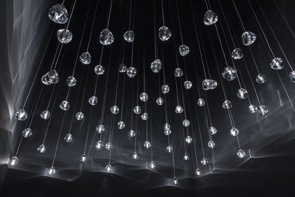 Scattered clear glass heads on this Clérachic pendant hang on thin wires in a black space, with soft light streaks behind.