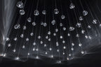 Scattered clear glass heads on this Clérachic pendant hang on thin wires in a black space, with soft light streaks behind.