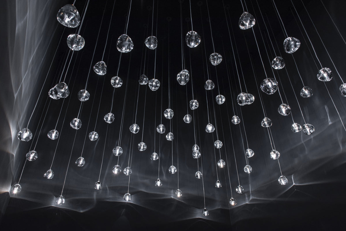Scattered clear glass heads on this Clérachic pendant hang on thin wires in a black space, with soft light streaks behind.
