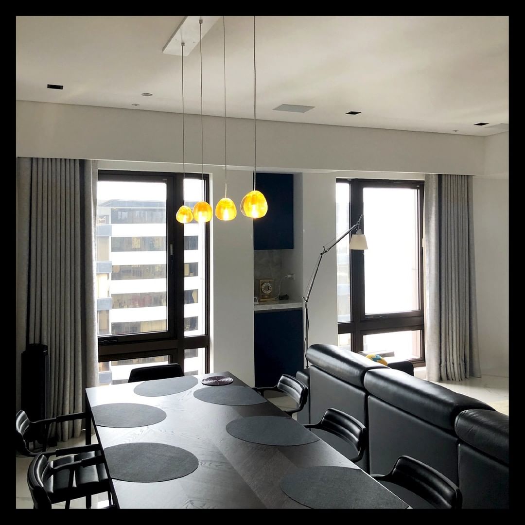 Over a dark dining table in a grey room with tall windows, this Clérachic pendant hangs as a short row of amber glass heads.