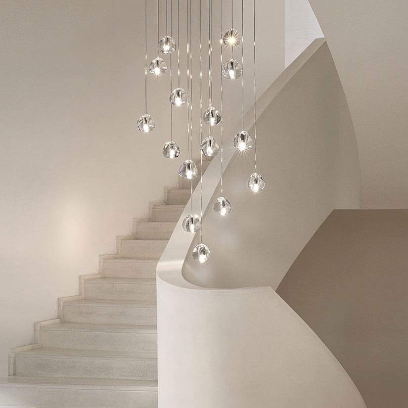 A Clérachic pendant cluster of clear glass heads hangs down beside a curving white stair, each head at a different height.