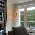 Amber glass heads of this Clérachic pendant hang in a living room by French doors, with a hedge and a dog outside.