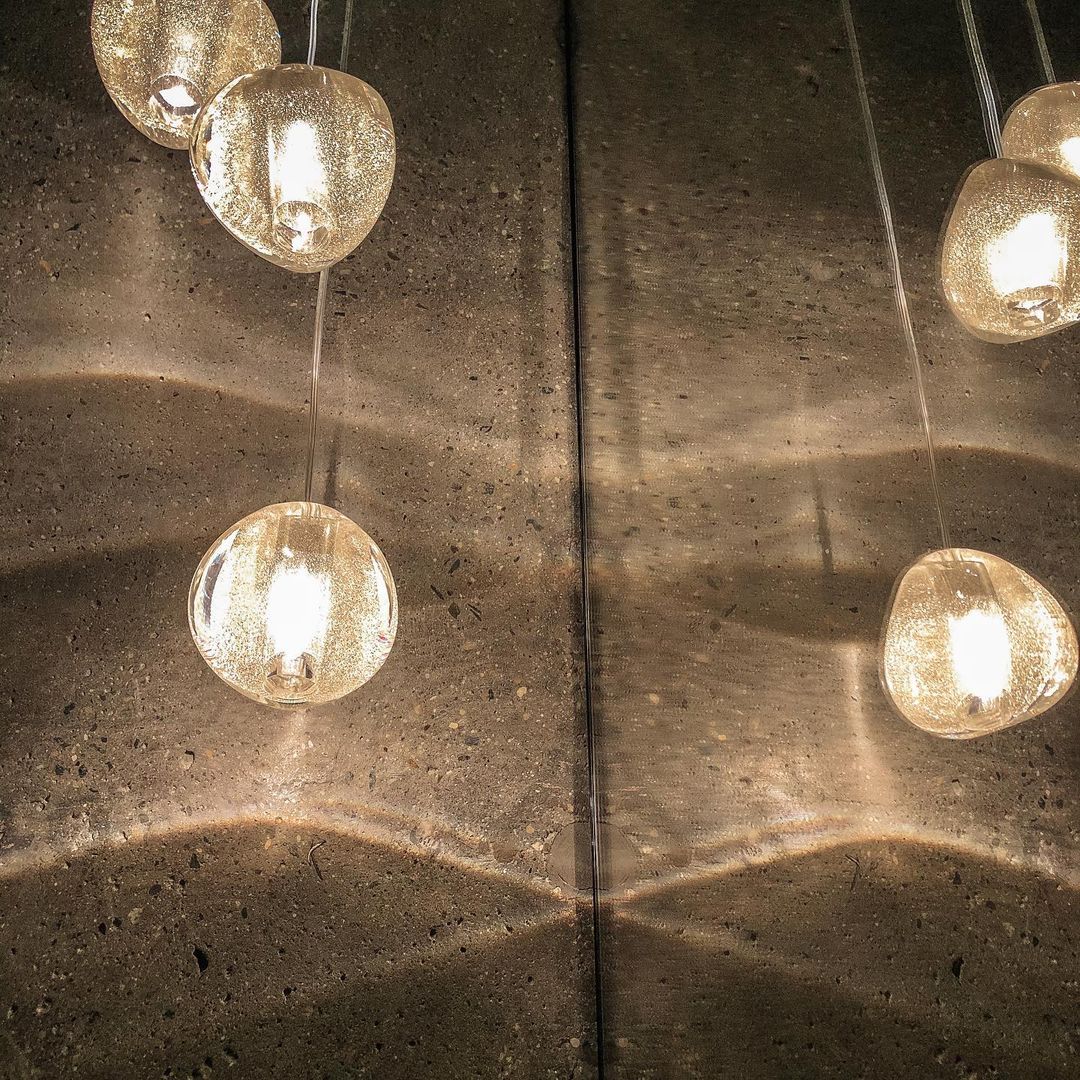 Close view of pale gold glass heads on this Clérachic pendant, with light rippling over a rough concrete wall.