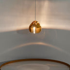 A single amber glass head from this Clérachic pendant glows against a pale wall, above a curved gold-toned rim below.