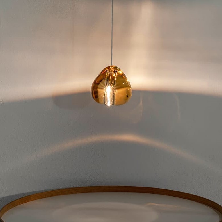 A single amber glass head from this Clérachic pendant glows against a pale wall, above a curved gold-toned rim below.