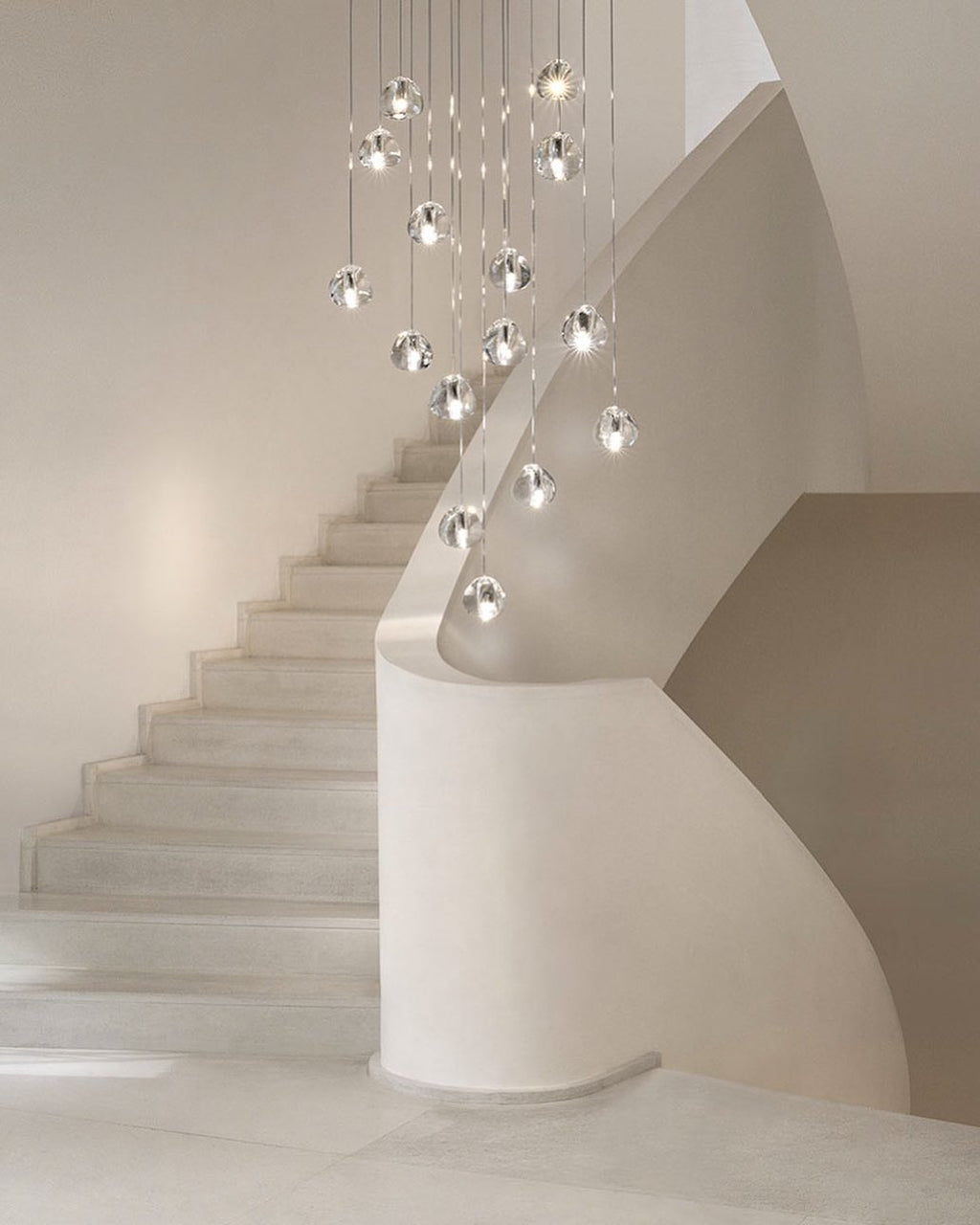 A Clérachic pendant with clear glass heads hangs at varied heights beside a pale curved staircase.