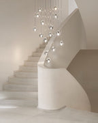 A Clérachic pendant with clear glass heads hangs at varied heights beside a pale curved staircase.