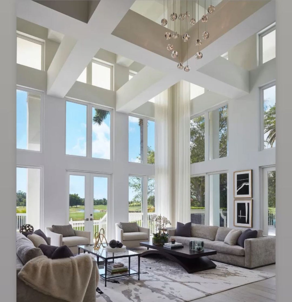 High above a double-height living room with tall windows and a long sofa, this Clérachic pendant hangs as a distant cluster.