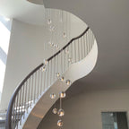 A Clérachic pendant with clear glass heads hangs over a spiral stair with a slim handrail, ending low above the landing.