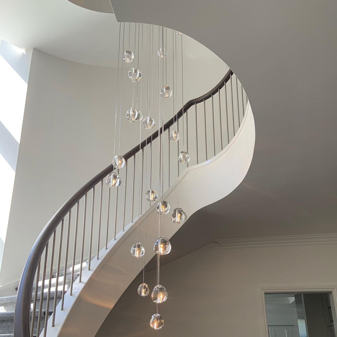 A Clérachic pendant with clear glass heads hangs over a spiral stair with a slim handrail, ending low above the landing.