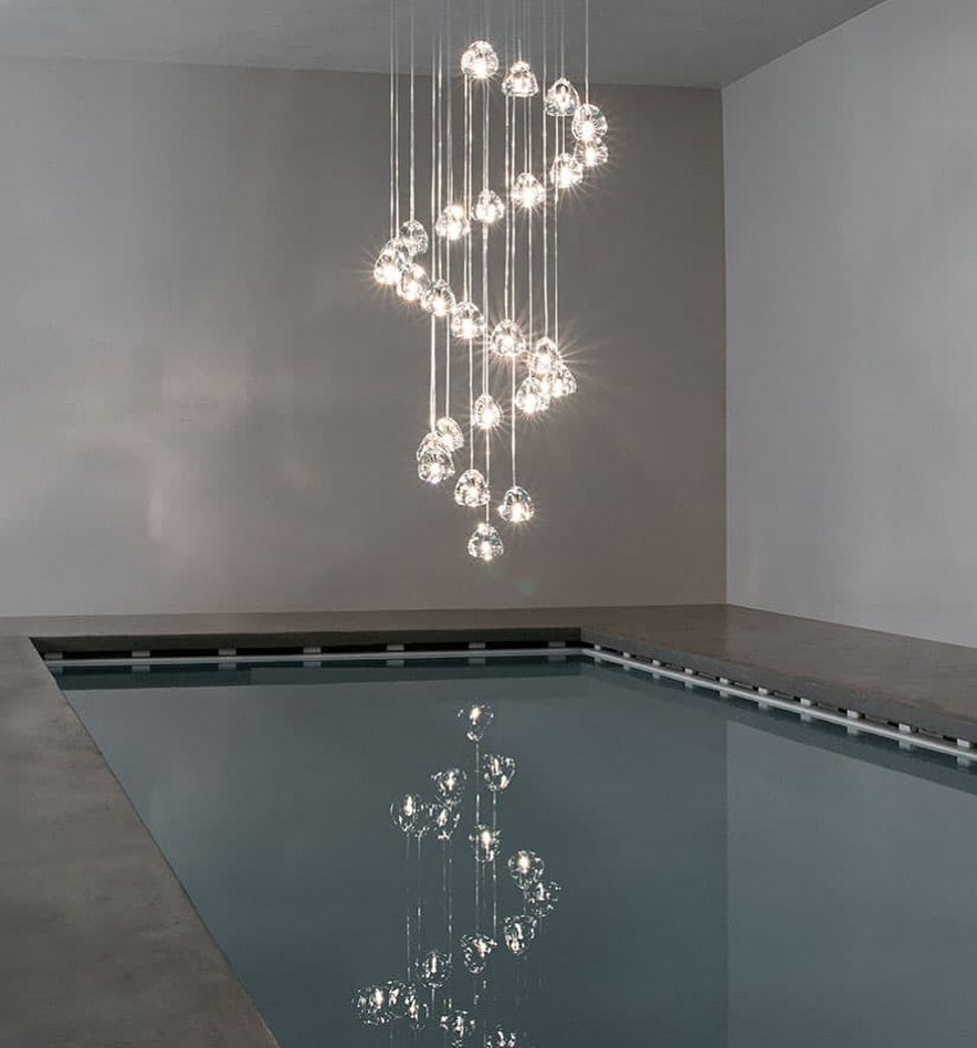 This Clérachic pendant winds in a spiral of clear glass heads above an indoor pool, with a still reflection on the water.