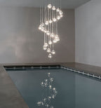 This Clérachic pendant winds in a spiral of clear glass heads above an indoor pool, with a still reflection on the water.