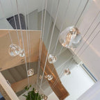 Looking down a stairwell with pale wooden stair flights, a Clérachic pendant's clear glass heads hang close to the camera.