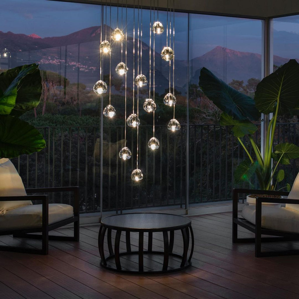 At dusk on a terrace with a mountain view, this Clérachic pendant hangs as a tall cluster of clear heads above a round table.