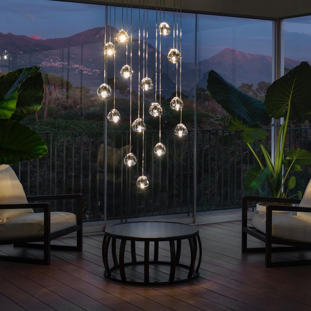At dusk on a terrace with a mountain view, this Clérachic pendant hangs as a tall cluster of clear heads above a round table.