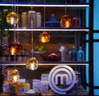 Amber glass heads of this Clérachic pendant hang in front of shelves of food jars and boxes, lit from within.