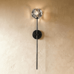 Clérachic black wall sconce, a faceted crystal shade on a long slim stem, glowing against a warm limewash wall.