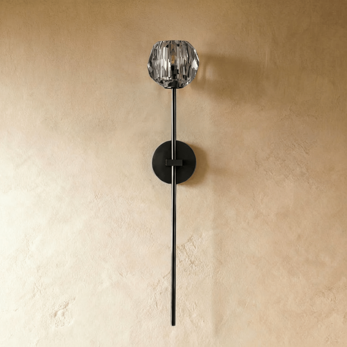 Clérachic black wall sconce with a faceted crystal shade on a long thin stem and round plate, switched off on a plaster wall.