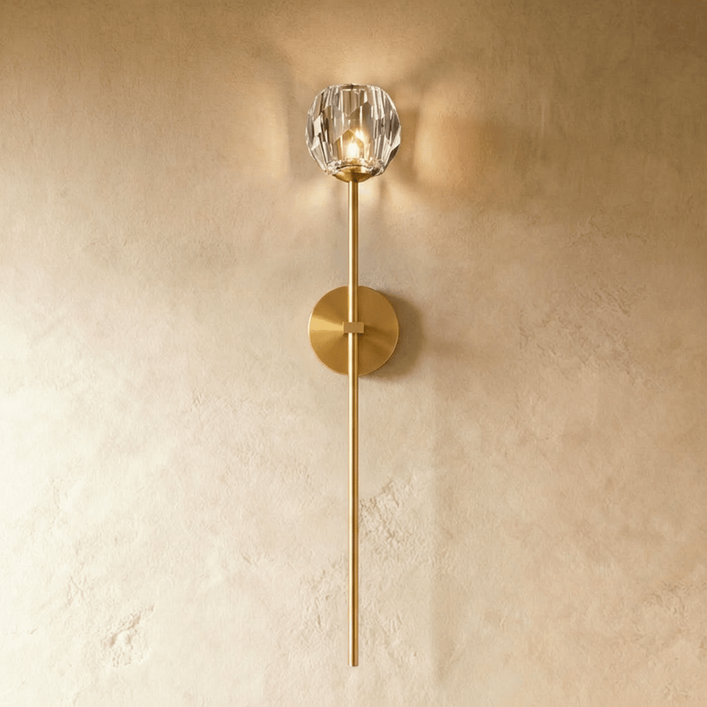 Clérachic gold wall sconce, a faceted crystal shade lit warm on a long brass-toned stem and round wall plate.