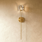 Clérachic gold wall sconce, a faceted crystal shade lit warm on a long brass-toned stem and round wall plate.