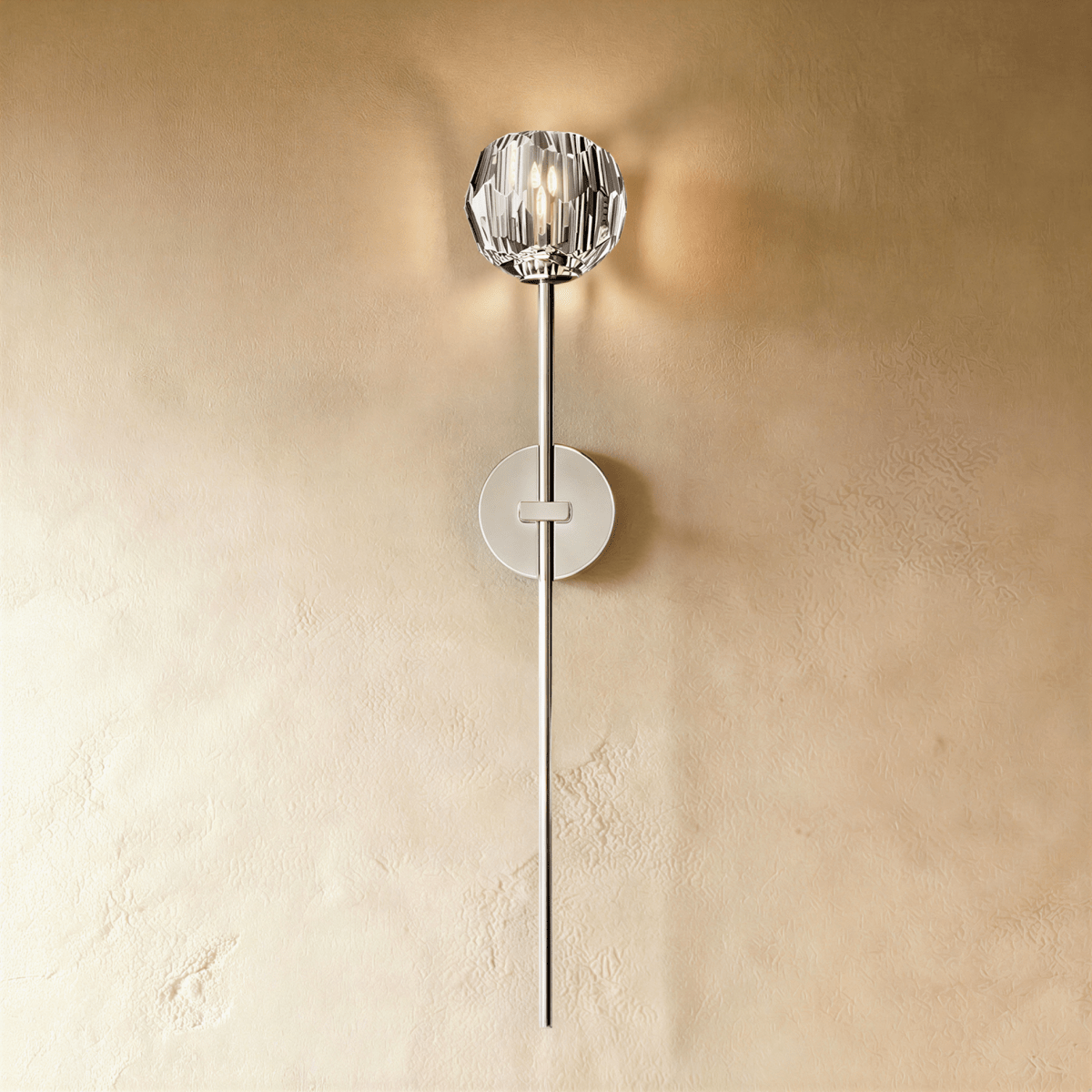 Clérachic silver wall sconce with a faceted crystal shade on a long polished stem, glowing on a warm plaster wall.