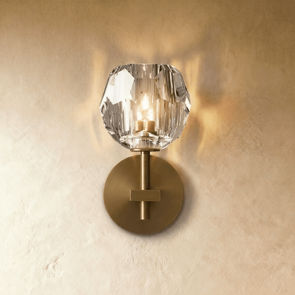Clérachic short gold wall sconce, a faceted crystal shade glowing warm above a brushed brass round wall plate.