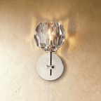 Clérachic short silver wall sconce, a lit faceted crystal shade over a polished round wall plate on plaster.