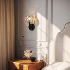 Clérachic black wall sconce with a faceted crystal shade on a panelled wall above a bedside table and dried flowers.