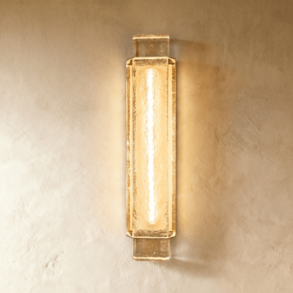 Clérachic tall rectangular wall light of rippled gold-toned glass with a bright central tube, lit on a plaster wall.