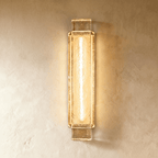 Clérachic tall rectangular wall light of rippled gold-toned glass with a bright central tube, lit on a plaster wall.