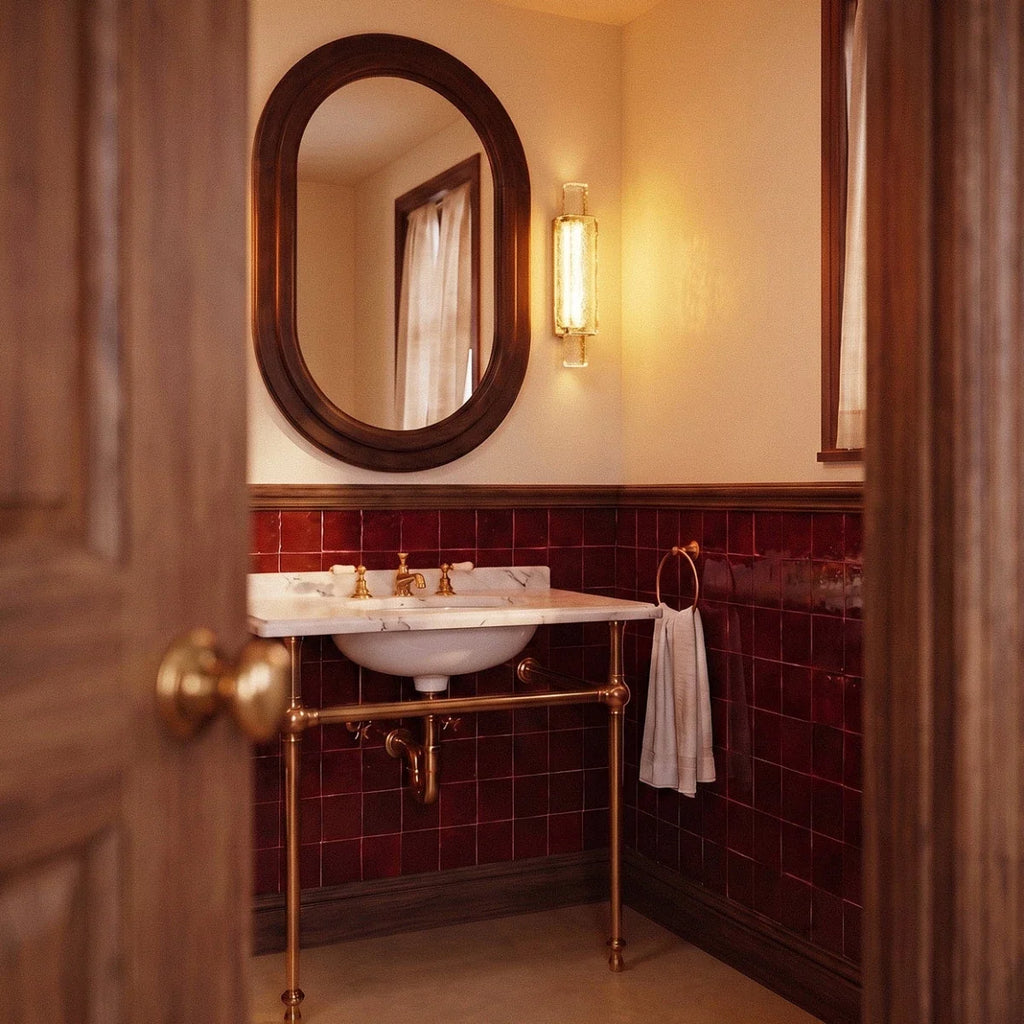 Clérachic slim gold and crystal wall light lit beside an oval mirror in a tiled room with deep red tiles and brass taps.