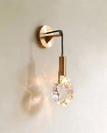 Clérachic crystal wall sconce, a rough-cut glass stone glowing warm on a slim brass arm against a plain wall.