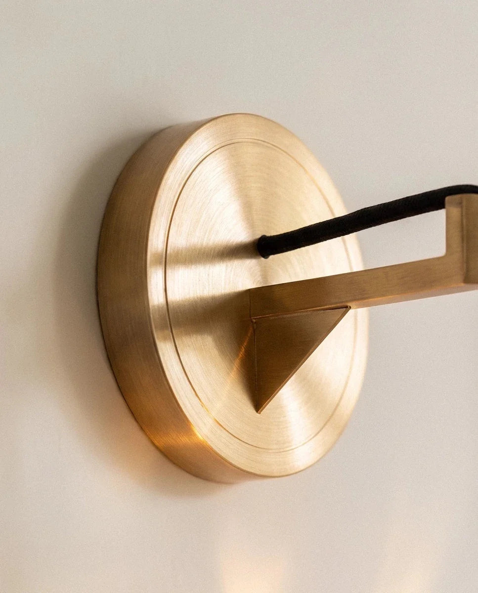 Close-up of the Clérachic crystal wall sconce's brushed brass wall plate and angled arm, black cord visible.