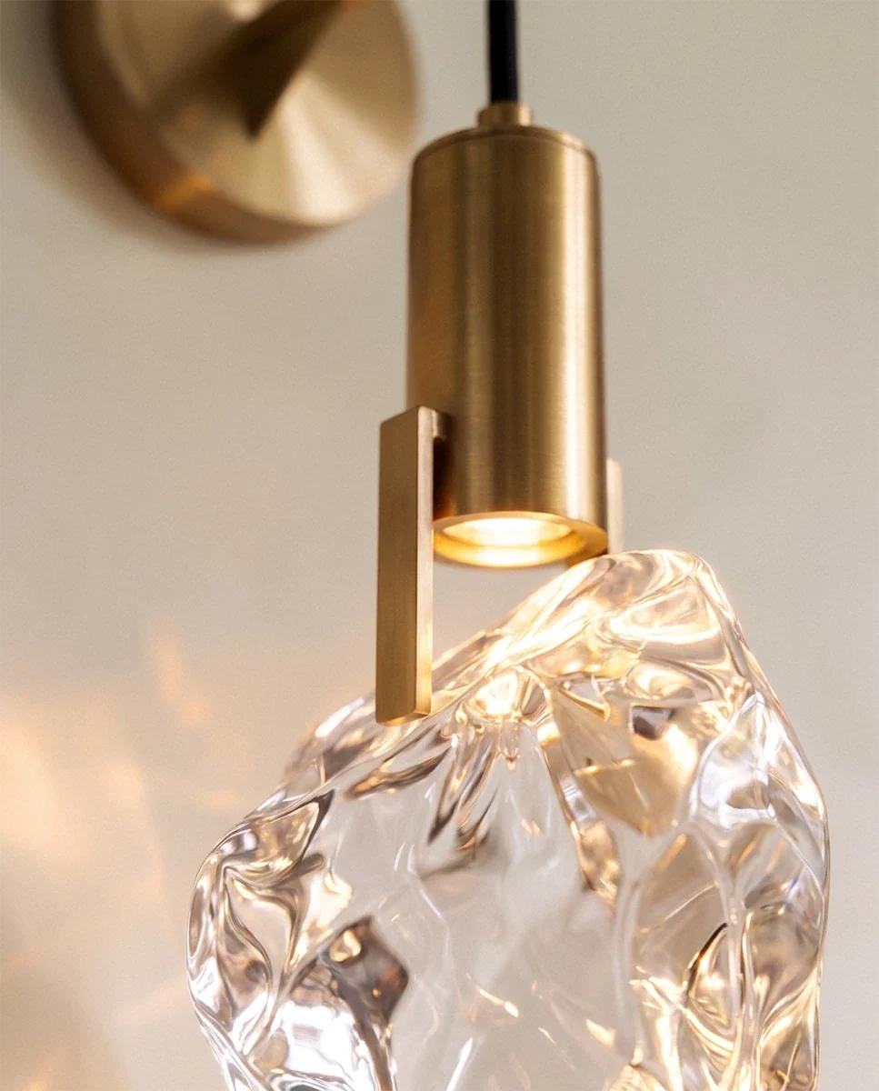 Close-up of the Clérachic crystal wall sconce's rough-cut glass stone lit warm white beneath its brass mount.
