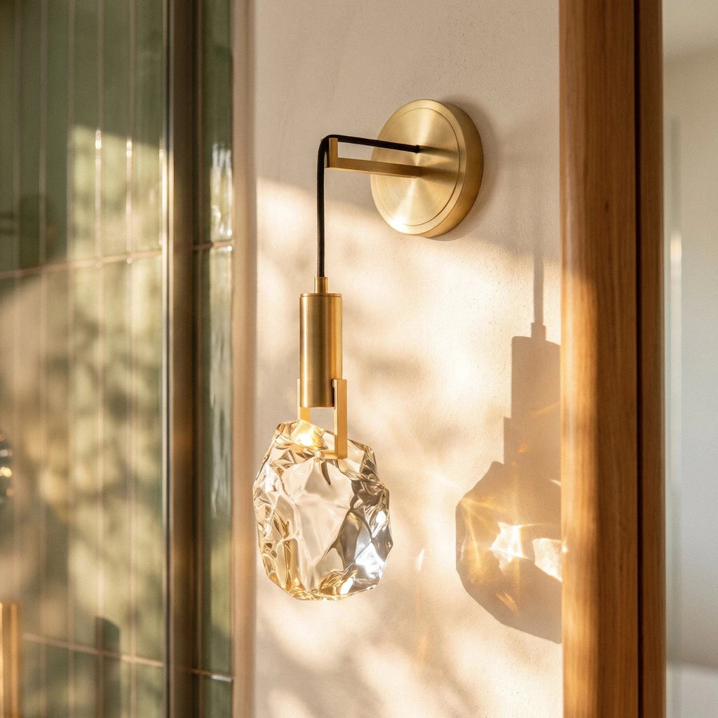 Close-up of the Clérachic crystal wall sconce's glass stone glowing warm beside a wood-framed glass door.