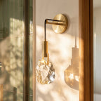 Close-up of the Clérachic crystal wall sconce's glass stone glowing warm beside a wood-framed glass door.