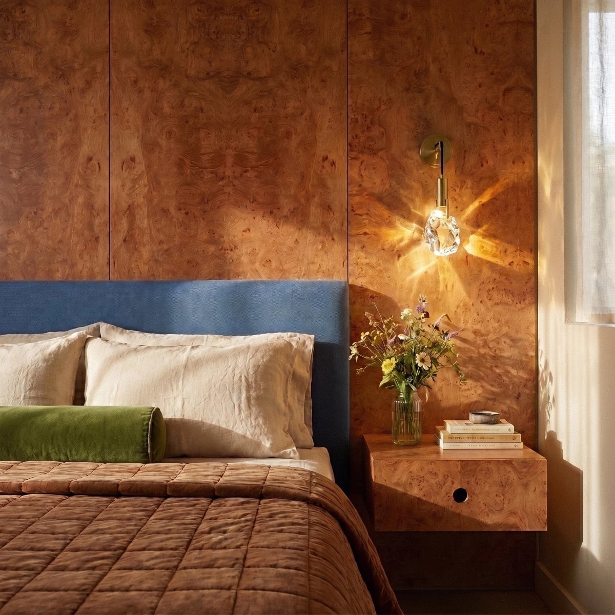 Clérachic crystal wall sconce glowing warm on a burl wood bedroom wall beside a floating nightstand.