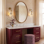 Two Clérachic crystal wall sconces flank an oval mirror above a glossy burgundy vanity with a marble top.