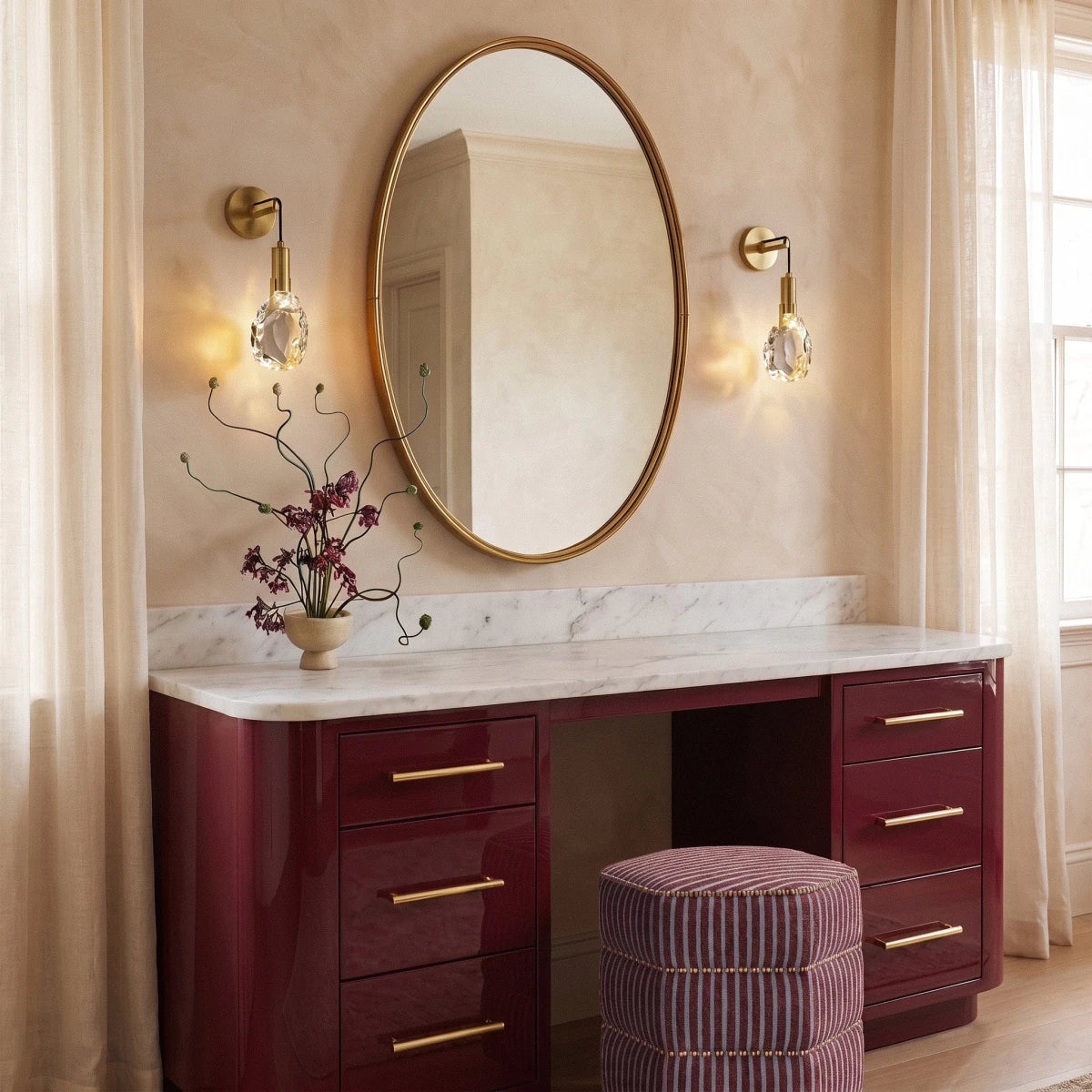 Two Clérachic crystal wall sconces flank an oval mirror above a glossy burgundy vanity with a marble top.
